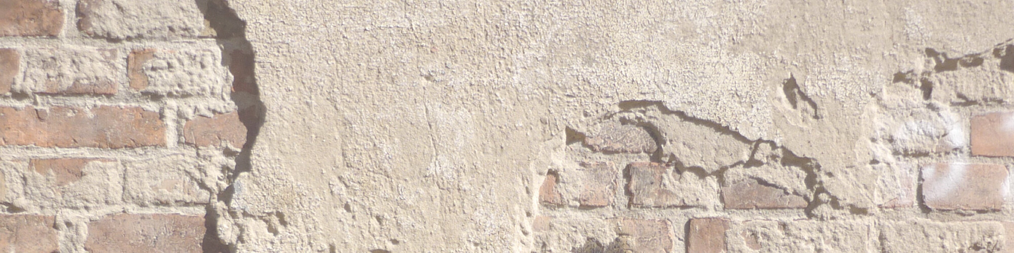 Eine alte Mauer aus Ziegelsteinen mit abgeplatztem Putz