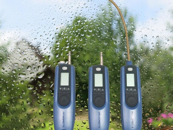 Three blue handheld moisture meters in front of a window with water droplets